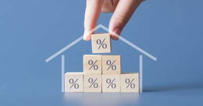 Construction of a house by hand by wooden cubics with the percent sign on them. Concept of interest rates,