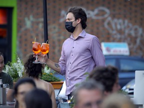 A masked bartender serves drinks on a terrace on Mount Royal Ave. in Montreal.