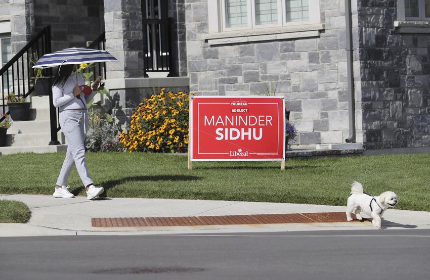 A woman walks her dog next to a poster for candidate Maninder Sidhu in Brampton East.