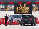 In this file photo, US customs officials talk to people in a car next to a sign that says the US border is closed at the US / Canada border in Lansdowne, Ontario, March 22, 2020.
