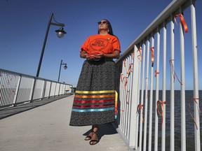Elayne Isaacs, cultural resource coordinator with Can-Am Indian Friendship Center is displayed on the Lakeside Park boardwalk on Wednesday, September 29, 2021. The town of Tecumseh tied 215 orange ribbons to commemorate the unnamed graves of indigenous children.  Isaacs poses with an orange stone with a message of hope for the future.