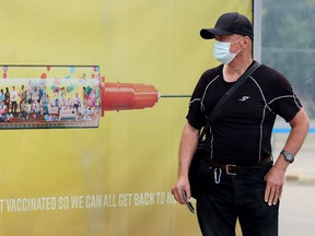 A transit passenger waits for his bus next to a COVID-19 vaccination announcement in Edmonton on July 17, 2021.