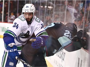 Seattle Kraken defender Carson Soucy (28) is slammed against the glass by Phillip Di Giuseppe (34) of the Vancouver Canucks in the second period during a preseason ice hockey game at the Spokane Veterans Memorial Arena.