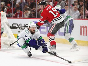 Conor Garland of the Vancouver Canucks removes the puck from Jonathan Toews of the Chicago Blackhawks at the United Center on October 21, 2021 in Chicago, Illinois.