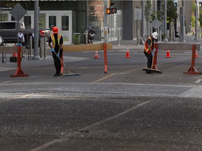 Workers clean pieces of broken glass along 102nd Street between 104th and 103rd avenues, from a pane of glass that fell from the Stantec tower on Friday, June 25, 2021.