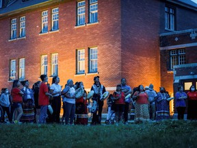Kamloops residents and First Nations people gather to listen to drummers and singers at a memorial in front of the former Kamloops Indian residential school after the remains of 215 children, some as young as three, were located. in the place.