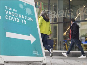 People walk past a sign advertising a COVID-19 vaccination site in Montreal, Sunday, Oct. 3, 2021.