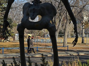 Two pedestrians walk between the bony legs of a skeleton decoration of at least 10 feet for Halloween in the front yard of a home in South Edmonton on October 19, 2021.