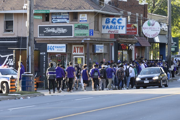 A group of students dressed in purple walk down a street in London, Ontario.
