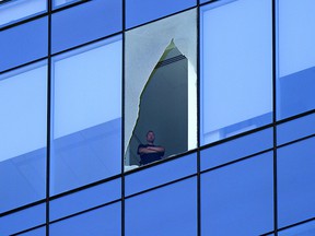 A man looks out of a broken window at the Stantec Tower in downtown Edmonton on Wednesday, July 28, 2021. Police closed the road at the base of the tower for hours while crews dealt with the problem.