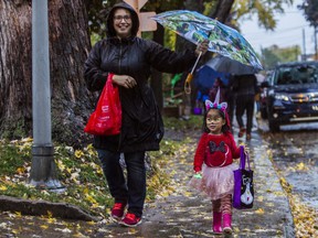 Caroline Mangerel holds an umbrella for her daughter Mireille on a soggy Halloween in the Montreal West area on Sunday.