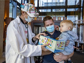 Toy Doctor Norman Brown gives a gift to 14-month-old Renaud Deshaies with her father Olivier at Shriners Hospital for Children in Montreal on Wednesday, Nov. 24, 2021.