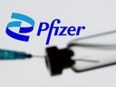 In this illustration, a syringe and vial are seen in front of a Pfizer logo.  PHOTO taken on June 24, 2021.