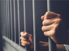 FILE PHOTO: Man in prison with his hands behind him holding steel bars in a cage.