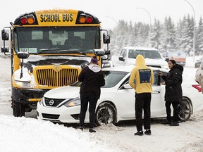 Drivers inspect for damage after a collision between an empty school bus and a car at the intersection of 50th Street and 44th Avenue in Edmonton on Tuesday, Nov. 16, 2021. The Phase 1 parking ban will begin at 7 p.m. and will remain in effect until the city has cleared major highways, such as arteries and collector roads, as well as expressways, bus routes, and roads with marking signs. 