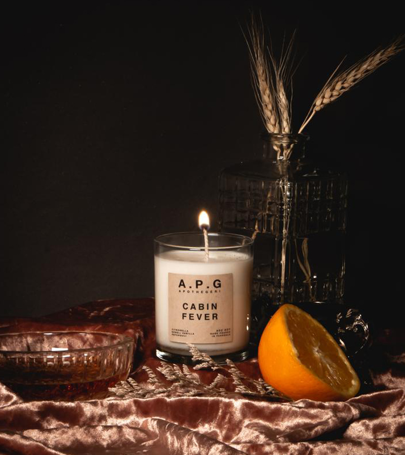 Photo of a white candle in a glass jar on a velvet cloth next to a sliced ​​orange 