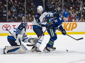 Winnipeg Jets goalkeeper Eric Comrie looks away as defender Dylan DeMelo controls Vancouver Canucks forward Vasily Podkolzin in the first period at Rogers Arena.