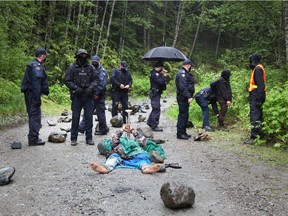 A woman plays a trumpet while lying on the road as RCMP officers gather during an operation to arrest protesters managing the Waterfall Camp blockade against logging old wood in the Fairy Creek area of ​​Vancouver Island at the beginning of this year.