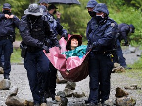 RCMP officers lead a woman they arrested at the Waterfall Camp blockade against logging old wood in the Fairy Creek area of ​​Vancouver Island on May 24, 2021.