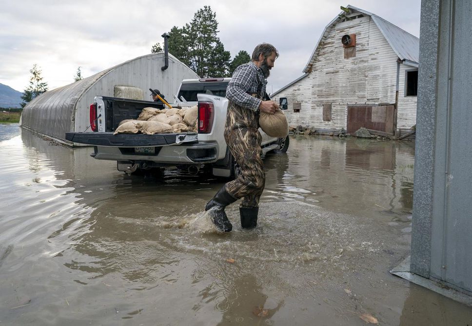 People carry sandbags to try to stop rising floodwaters in Barrowtown, near Abbotsford, BC on Friday.