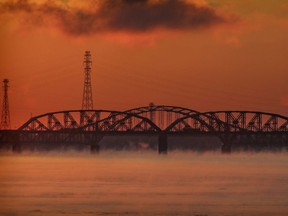 The sky is bathed in warm light behind the Mercier Bridge and the neighboring rail bridge at sunrise in Montreal on Monday, February 1, 2021.