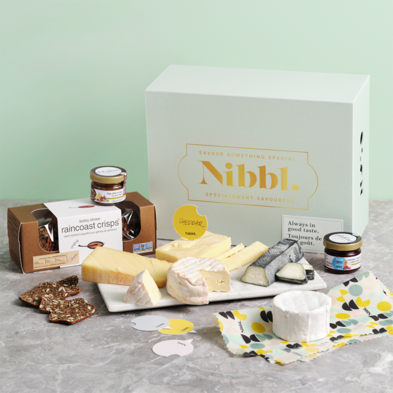 A box of Nibbl cheese with various cheeses and crackers scattered on a plate 