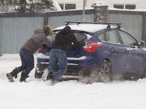 Good Samaritans push a trapped motorist at the intersection of 38th Avenue and 38th Street, in Edmonton, on Tuesday, November 16, 2021. The City of Edmonton's phase 1 parking ban will begin at 7 pm and remain effective until the city has cleared major highways such as arterial and collector roads, as well as highways, bus routes, and highways with 