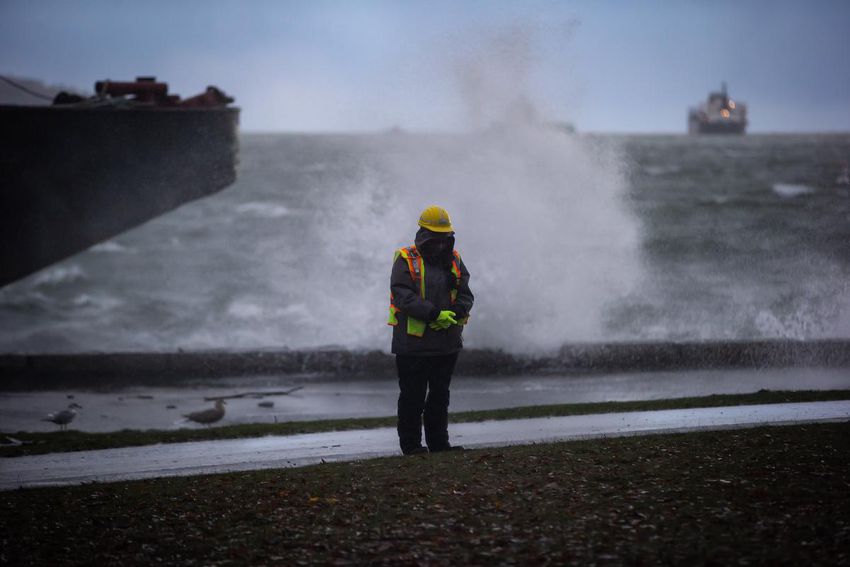 Waves crash over the seawall behind a worker trying to direct people around a flooded part of the seawall during a massive windstorm in Vancouver.