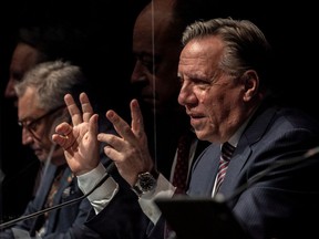 Quebec Prime Minister François Legault, accompanied by Public Health Director Horacio Arruda, with Health Minister Christian Dubé seen in a reflection, during a press conference on COVID-19 in Montreal on Wednesday, December 22, 2021 .