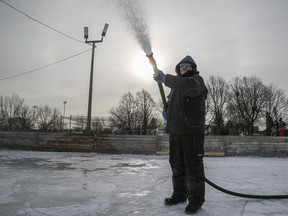 With the low winter sun in the background, Montreal city worker Yves sprays water on a hockey rink in Beaubien Park on Monday, Dec. 27, 2021.