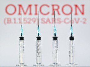 An illustration image taken in London on December 2, 2021 shows four syringes and a screen displaying the word 'Omicron', the name of the new variant of covid 19.