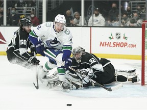 Vancouver Canucks' Quinn Hughes, center, goes after the puck deflected by Los Angeles Kings goalkeeper Jonathan Quick during the first period of an NHL hockey game Thursday, Dec. 30, 2021, in Los Angeles.