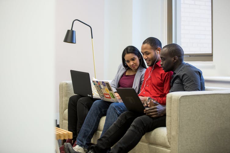 Three racialized youth laugh as they look at their laptops.