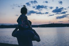 A girl sits on her father's shoulders as they watch a sunset.