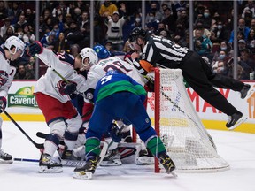 Referee Trevor Hanson, right, jumps over the net to search for the puck as Vancouver Canucks 'Tanner Pearson (70) and JT Miller (9) search for it against Columbus Blue Jackets' Boone Jenner (38) and Jake Bean (22) .  ) under goalie Elvis Merzlikins during the second period of an NHL hockey game in Vancouver, Tuesday, Dec. 14, 2021.