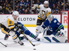 Pittsburgh Penguin Evan Rodrigues hits the puck in front of Vancouver Canucks goalkeeper Thatcher Demko as Penguins captain Sidney Crosby watches during the first period of their game Saturday night at Rogers Arena.
