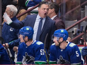 Canucks head coach Travis Green behind the bench, while defenders Tyler Myers and Tucker Poolman (right) follow the play during the first period of their NHL game on Dec. 4, 2021 against the Pittsburgh Penguins at the Rogers Arena.