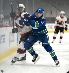 Canucks defender Quinn Hughes pushes Ottawa Senators forward Josh Norris across the boards during a Rogers Arena game in January 2021.