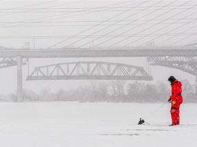 Charles Hu fishes the St. Lawrence River under the shadow of the two Champlain bridges in Brossard on Friday, January 7, 2022. The central span of the original bridge is lowered behind the new one.