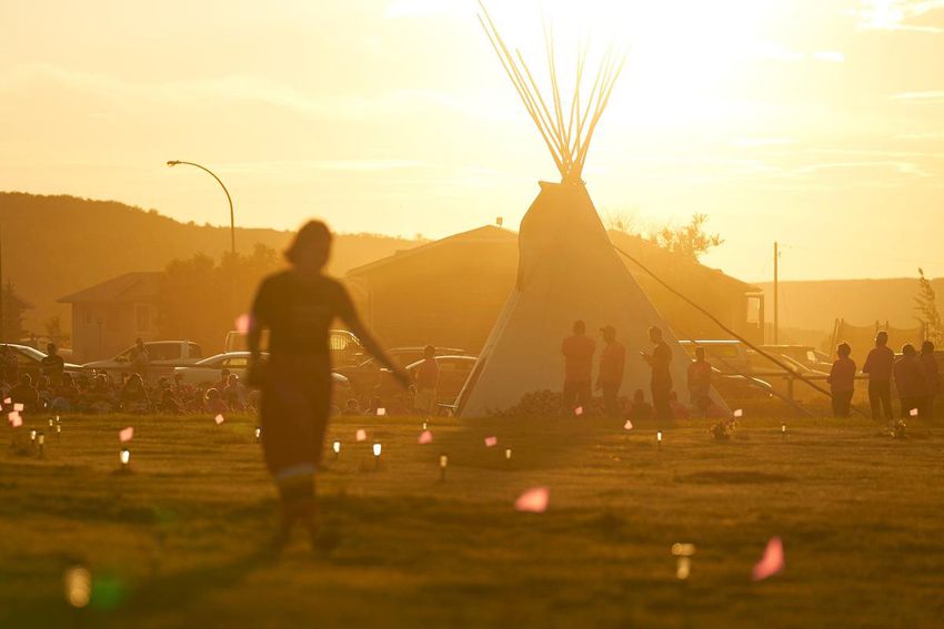 A woman walks through a field where flags and solar lights now mark the site where human remains were discovered in unmarked graves at the site of the former Marieval Indian Residential School in Cowessess First Nation, Sask., June 26, 2021 .