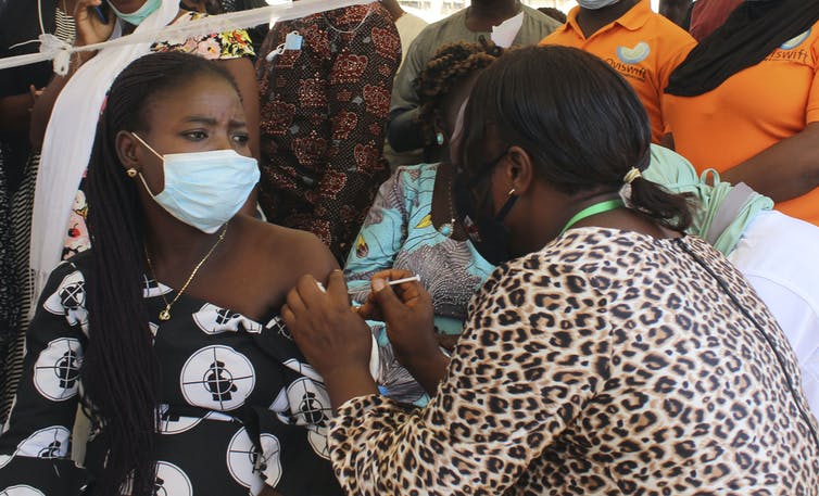 A black woman wearing a mask receives a COVID-19 vaccine from a nurse.