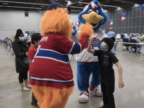 Kyle Appleby gets a high-five from Montreal Canadiens mascot Youppi!  at the Palais des congrès vaccine clinic on Feb. 5, 2022. Laval Rocket mascot Cosmo was also there to help make the experience easier for kids.