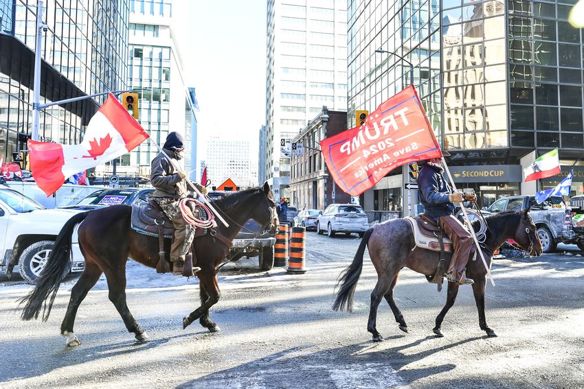 Two Freedom Convoy supporters, one holding a Trump flag, ride horses down Metcalfe Street on February 5, 2022 in Ottawa, Canada.
