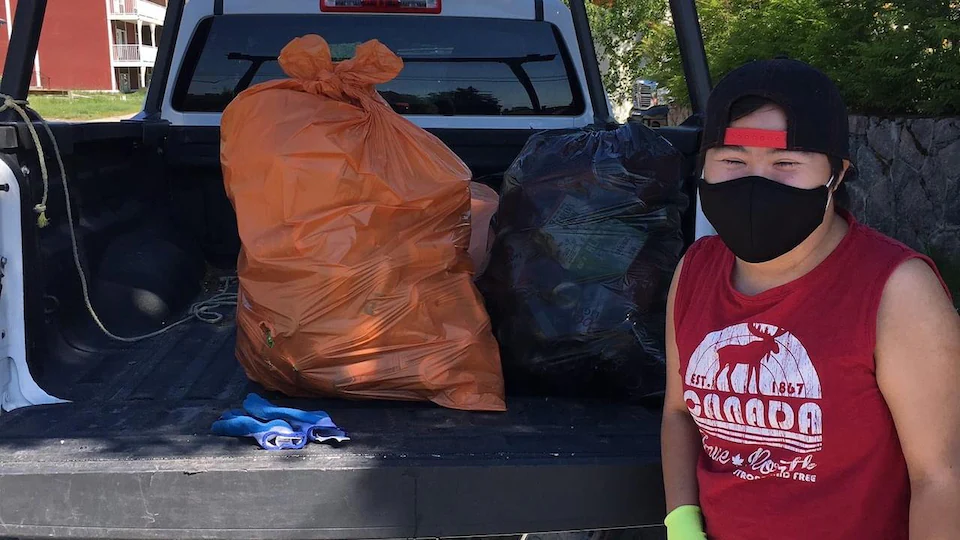 Une personne se tient devant des sacs de déchets chargés sur une camionnette.