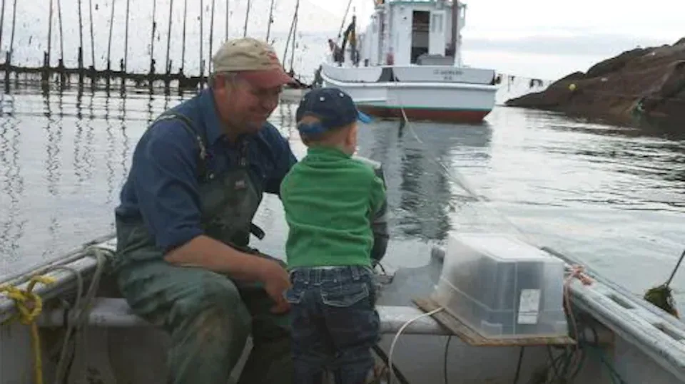 Un pêcheur dans une barque regarde son petit garçon en souriant.