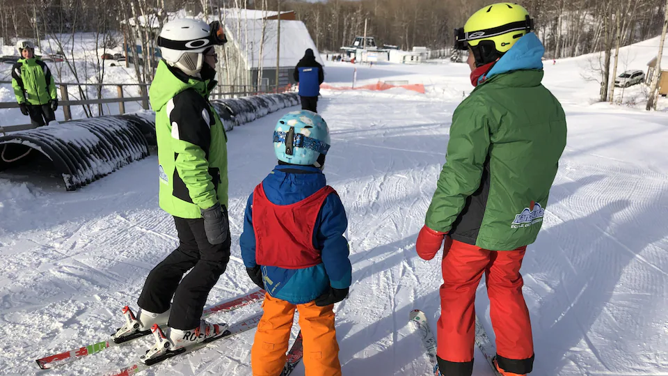 Deux adolescentes montrent à un enfant à skier.