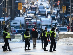 A protester carrying an empty fuel container on a broom handle walks past Ontario Provincial Police officers, as a protest against COVID-19 restrictions that has been marked by gridlock and the sound of truck horns continues into its second week in Ottawa on Monday, Feb. 7, 2022.