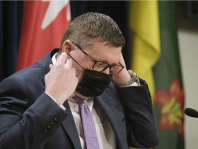 Premier Scott Moe puts a mask on during a press conference at the Legislative Building.