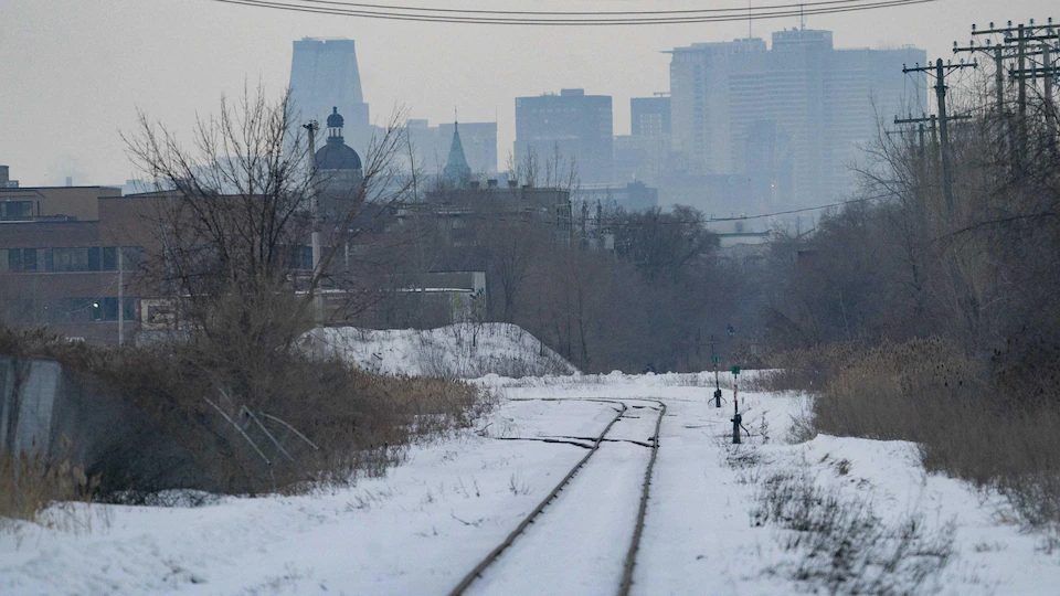 Une voie ferroviaire. En arrière-plan, le centre-ville de Montréal.

