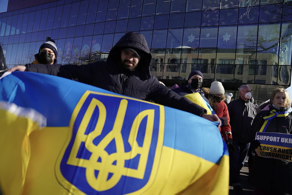 A man displays a yellow and blue flag decorated with the Ukrainian coat of arms in a public square.
